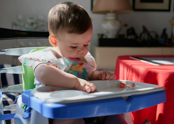 Cute toddler having tomatoes in his high chair for lunch