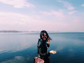 Portrait of young woman standing at shore against sky