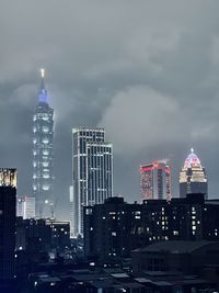 Illuminated buildings in city against cloudy sky