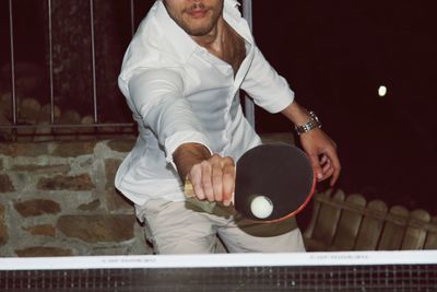 Midsection of man playing table tennis at night