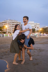 Portrait of girl standing with brothers at beach during dusk
