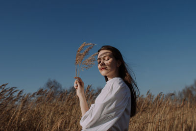 Beautiful woman standing on field against clear blue sky