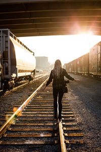 Rear view of woman walking on railroad track on sunny day