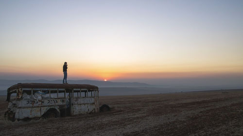 Silhouette person standing on field against sky during sunset