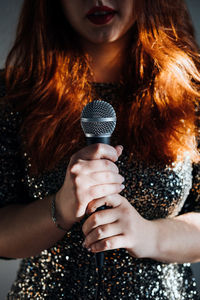 Faceless portrait of redhead woman in sparkly evening dress holding microphone on dark night