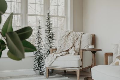 Chair with soft blanket and cup of coffee on small table in white room