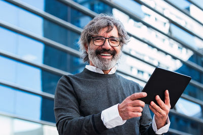 Happy businessman with digital tablet outside office building