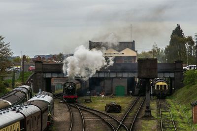 Steam train emitting smoke at shunting yard against sky