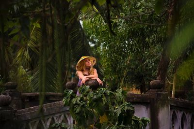 Full length of woman sitting on plant against trees