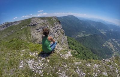 Rear view of woman crouching on cliff against sky