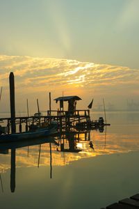 Silhouette fishing boat moored in sea against sky during sunset