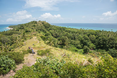 High angle view of people hiking on green mountain by sea