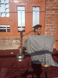 Young man sitting with hookah against window