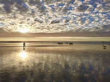 People walking on sea shore against sky during sunset