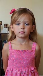 Portrait of girl in pink dress standing against wall at home