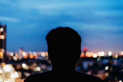 Rear view of silhouette man against illuminated city