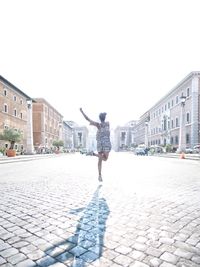Rear view of woman jumping on street against clear sky