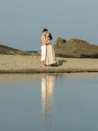 Young couple kissing while standing at beach against sky