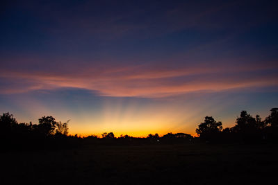 Silhouette trees on field against sky during sunset