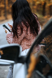 Confident brunette woman standing near car and call phone. preparing your car for fall autumn