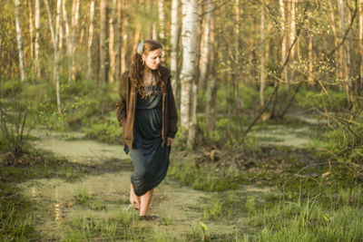 Woman walking in swamp against trees at forest