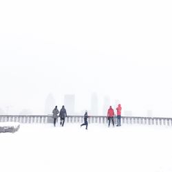 People walking on snow covered landscape against clear sky