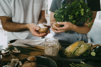 Midsection of male and female entrepreneurs holding mushrooms by jar with seeds at studio kitchen