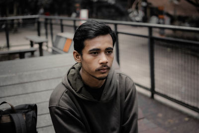 Portrait of young man sitting on railing