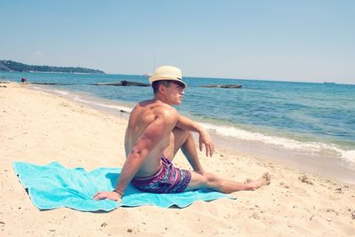 Shirtless man relaxing at beach against clear sky