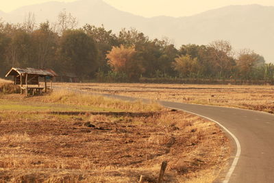 Road by trees on field against sky