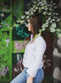 Profile view of young woman smoking while standing against graffiti wall