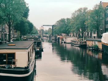 Boats moored in canal by city against sky