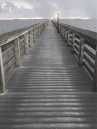 Empty wooden pier over sea against sky