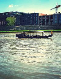 Boat sailing on river by buildings against sky