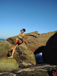 Woman sitting on rock against blue sky