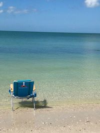 Empty chairs on beach against sky
