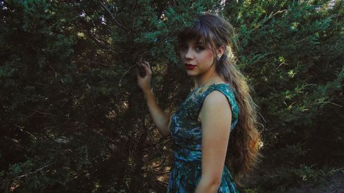 Portrait of young woman standing against tree