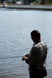 Rear view of man standing by lake and fishing