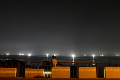 Rear view of boy sitting on seat against sea at night