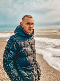 Portrait of mature man standing at beach against sky