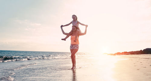 Full length of woman carrying happy daughter on shoulder at beach