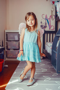 Portrait of cute girl wearing angel wings standing at home