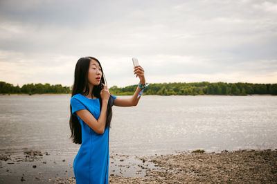 Woman taking selfie with smart phone by lake against sky