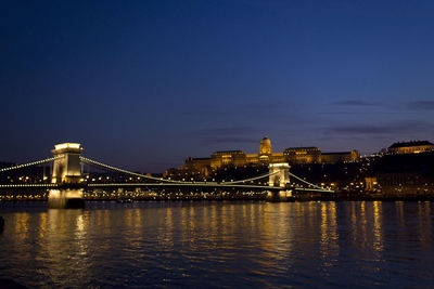 Illuminated bridge over river against sky at night