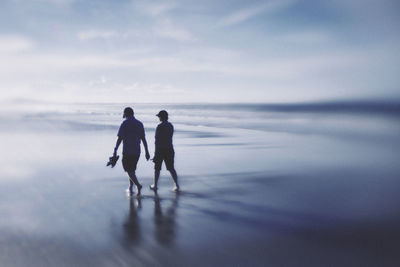 Men walking on beach against sky