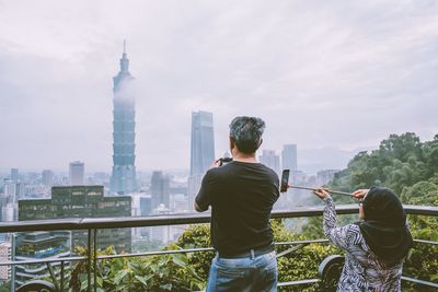 Rear view of man standing by railing against modern buildings