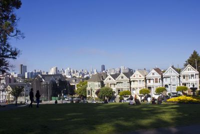 People in park by buildings against clear blue sky