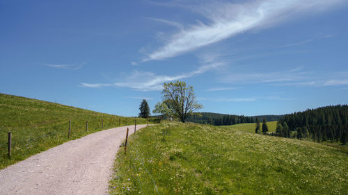 Empty road amidst field against sky