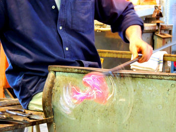 Midsection of worker spinning glass blower at factory