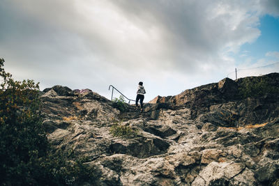 Man standing on rock by mountain against sky